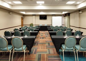 A conference room with rows of tables and chairs, a carpeted floor, and a whiteboard. - Hotel Indigo Chicago-Vernon Hills by IHG (Vernon Hills)