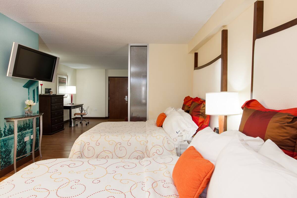 A hotel room with two beds, a TV, a desk, and a chair.