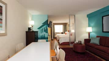 A hotel room with a dining table, two beds, a sofa, and a large window.
