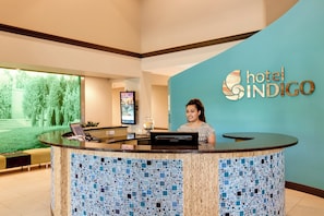 A hotel reception desk with a digital screen, a water dispenser, and a sign for 'hotel INDIGO'. - Hotel Indigo Chicago-Vernon Hills by IHG (Vernon Hills)