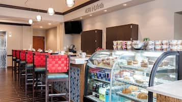 Una cafetería con mostrador, zona de estar y una vitrina con productos alimenticios.