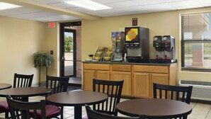 Un espace intérieur propre et bien éclairé, avec des tables et des chaises en bois, une machine à café et un distributeur automatique.