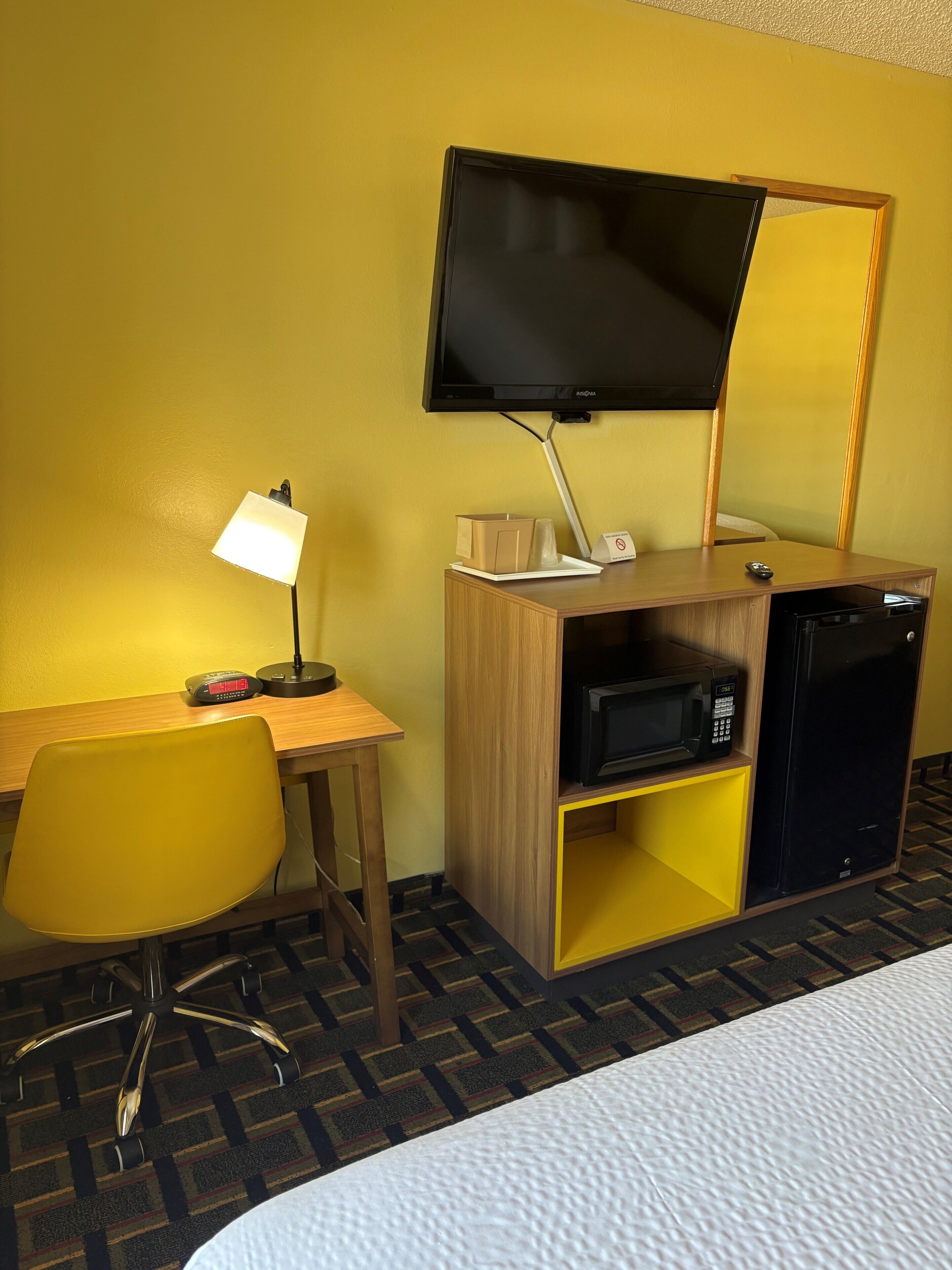 A hotel room with a desk, chair, television, microwave, and a bed.
