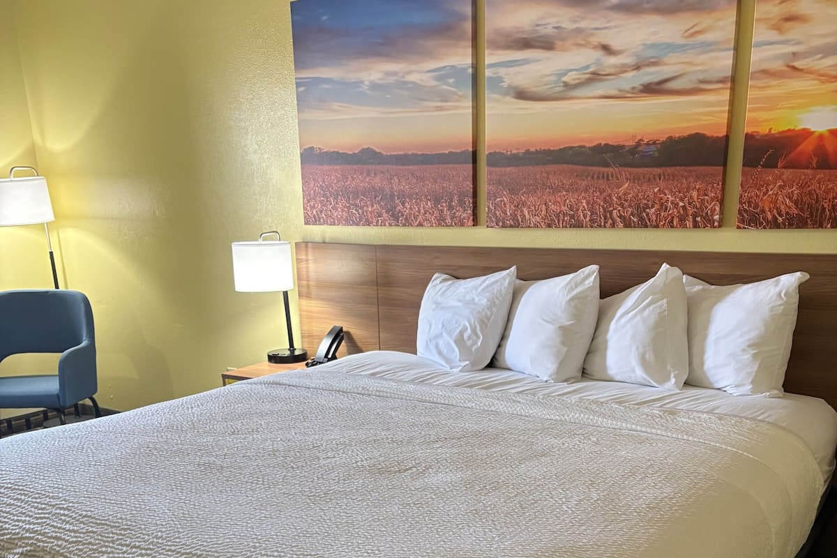 A hotel room with a large bed, a headboard, a desk with a lamp, and a chair.