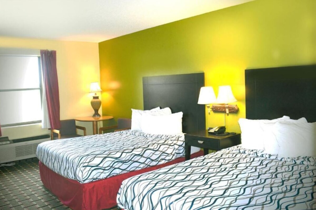 A hotel room with two beds, a small table, two lamps, a telephone, and a window with curtains.