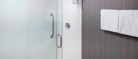 Una ducha con cerramiento de vidrio, una barra de apoyo, un perchero con una toalla blanca y una pared con diseño de líneas verticales.