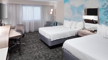 Una habitación de hotel con dos camas, un escritorio, una silla, un televisor y un ventanal con cortinas.