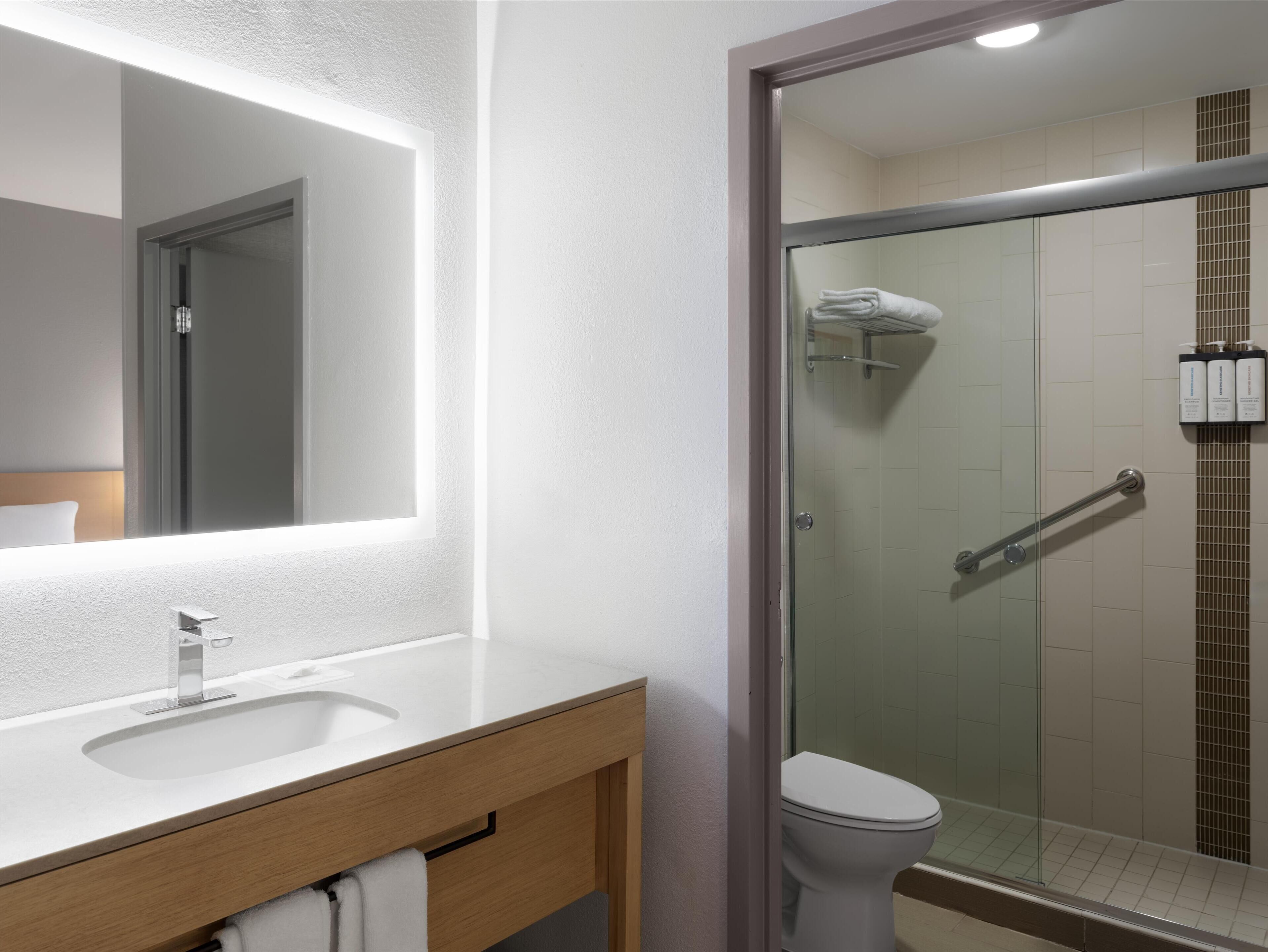A modern bathroom with a large mirror, a sink, and a glass-enclosed shower area.