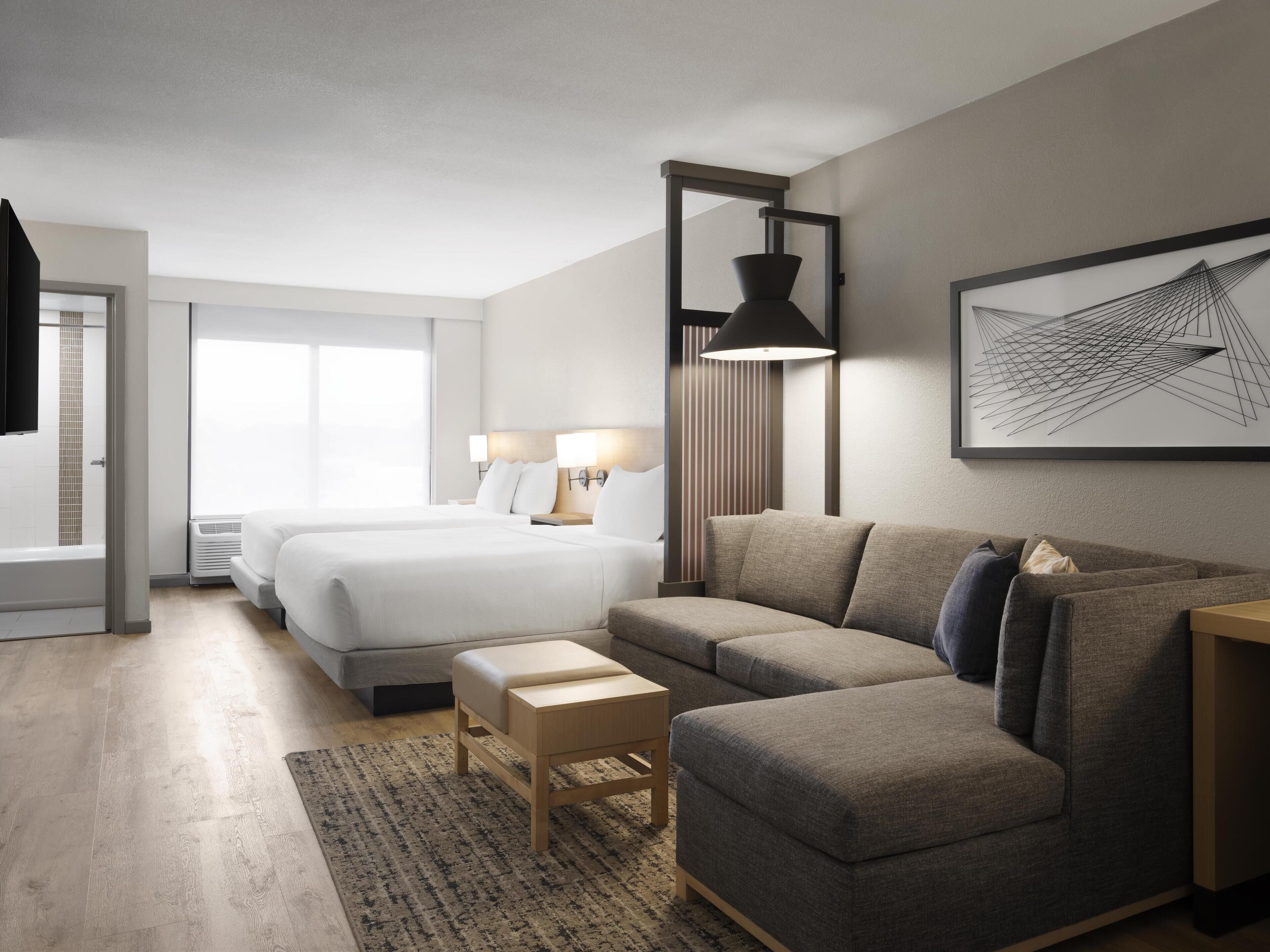 A modern hotel room with a large bed, a sofa, a small table, and a large window.