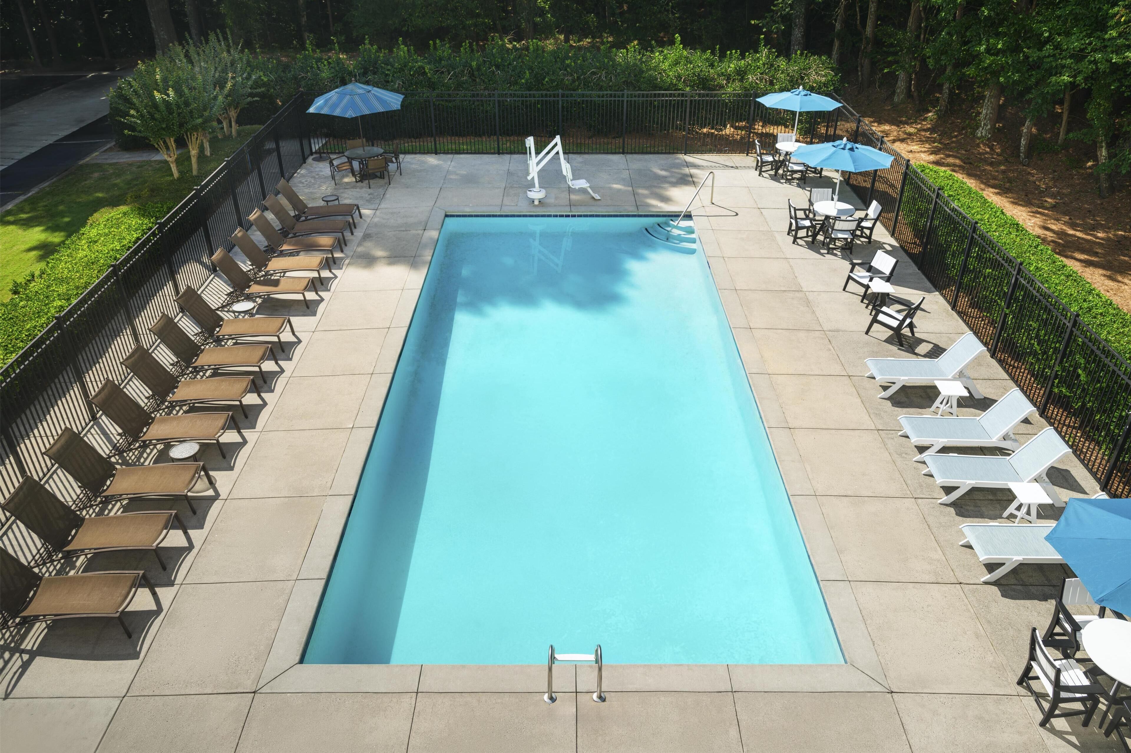 Una piscina rectangular con superficie de agua azul cristalina, rodeada de sillas de descanso y sombrillas.