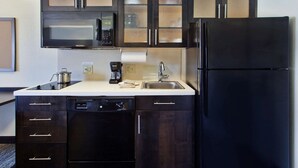 A compact kitchen with dark wood cabinets, a black refrigerator, a microwave, a coffee maker, and a dishwasher. - MainStay Suites Wichita Northeast (Wichita)