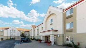 A multi-story hotel with a beige facade, a red roofline, and a parking lot with a single car. - MainStay Suites Wichita Northeast (Wichita)
