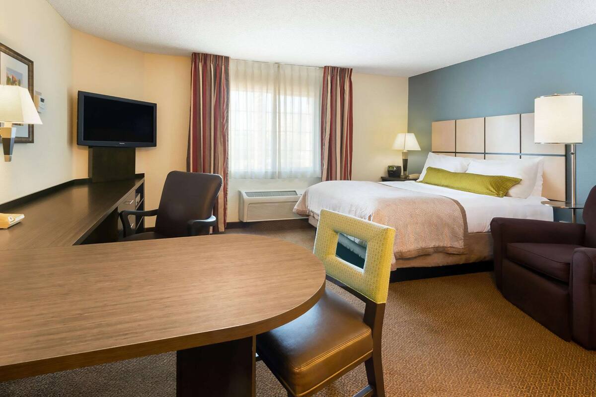 A hotel room with a bed, a desk, a chair, a television, and a window with curtains.