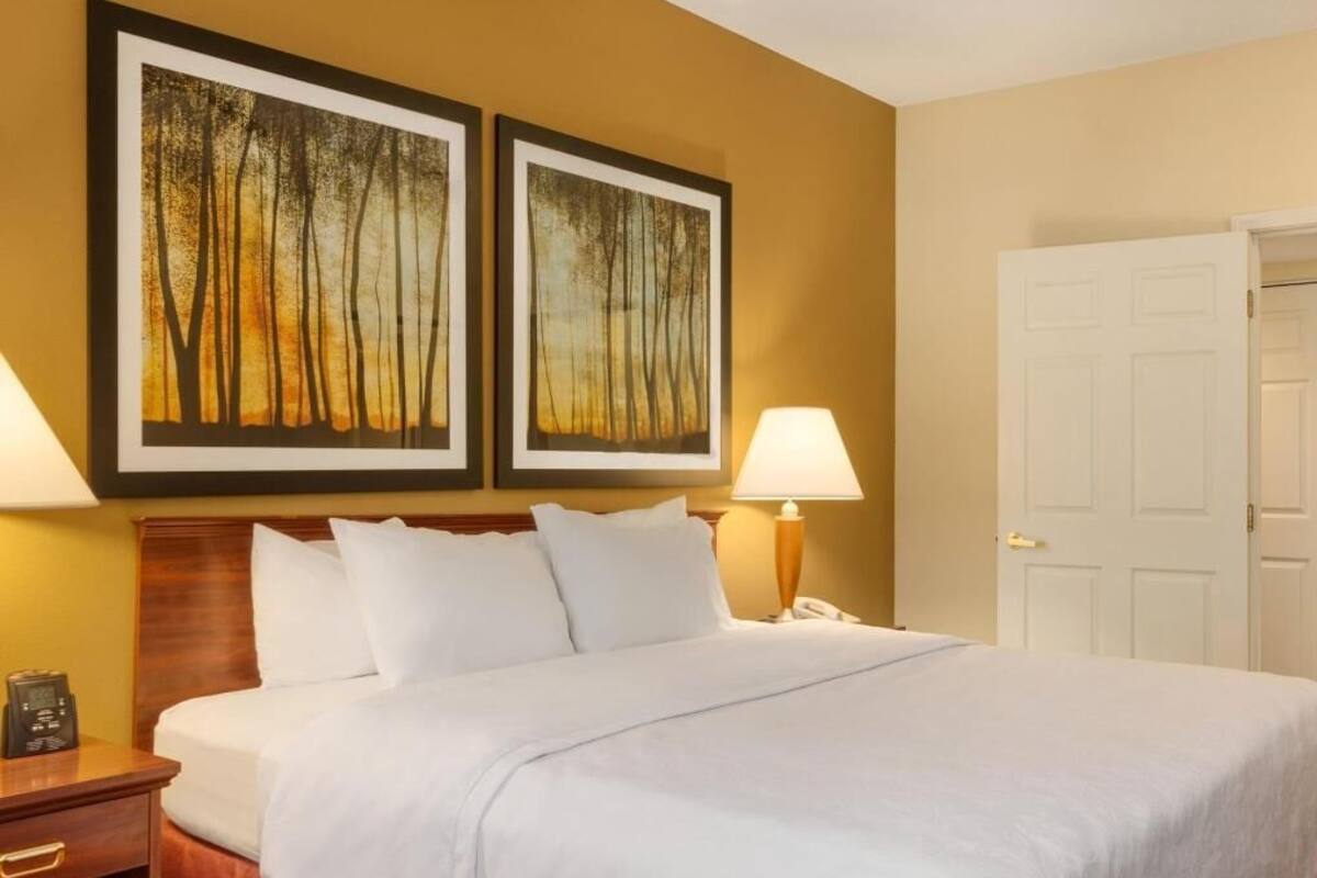 Een hotelkamer met een bed, twee wanddecoraties, een bedlamp, een nachtkastje en een deur.