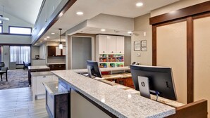 A hotel reception area with a counter, computers, and a kitchenette in the background. - Homewood Suites Kansas City/Overland Park (Overland Park)