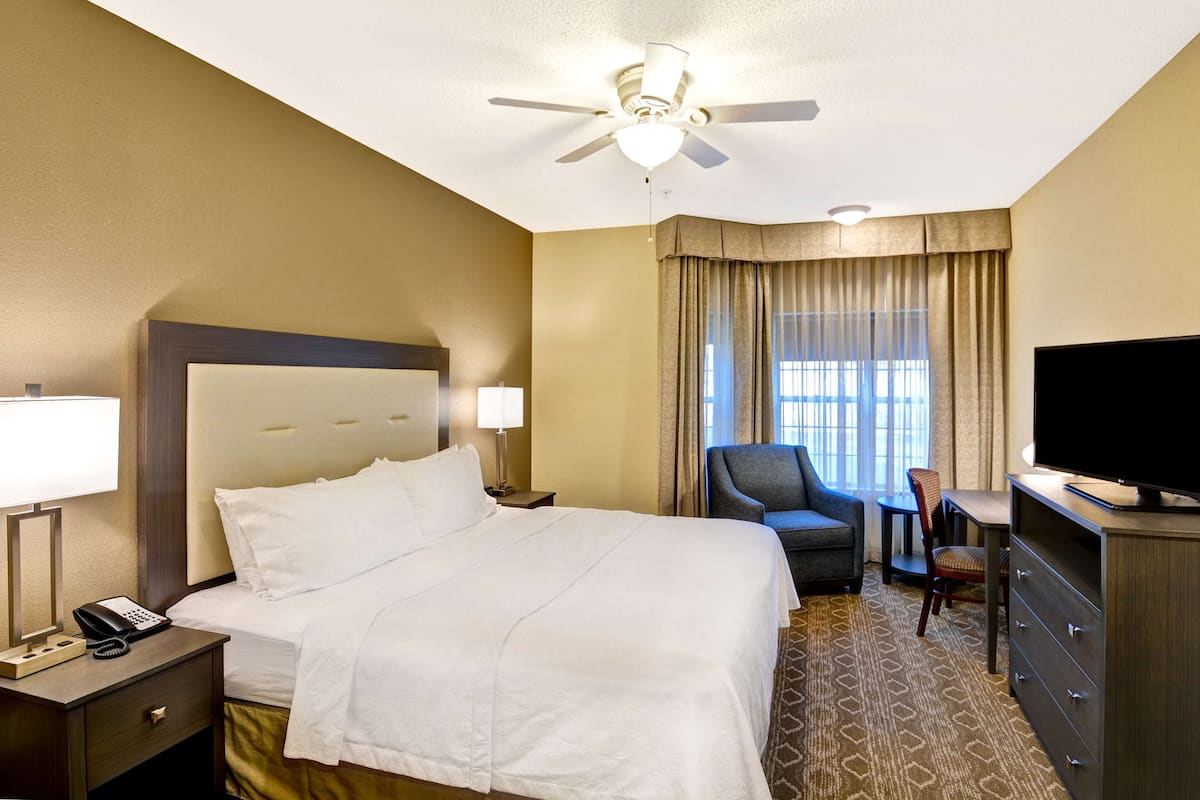 Una habitación de hotel con una cama, un escritorio, una silla, un televisor y un ventilador de techo.