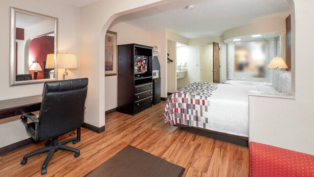 A hotel room with a bed, a desk with a chair, a television, and a bathroom visible through an archway. - Red Roof Inn & Suites Oxford (Oxford)