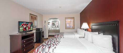 A hotel room with a large bed, a television, a dresser, a mirror, and a bedside table with a lamp.