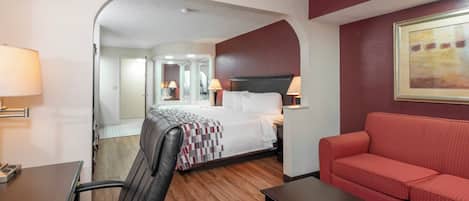 A hotel room with a bed, a red sofa, a desk, and a chair.