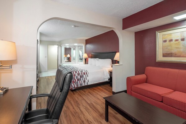 Une chambre d’hôtel avec un lit, un canapé rouge, un bureau et une chaise.