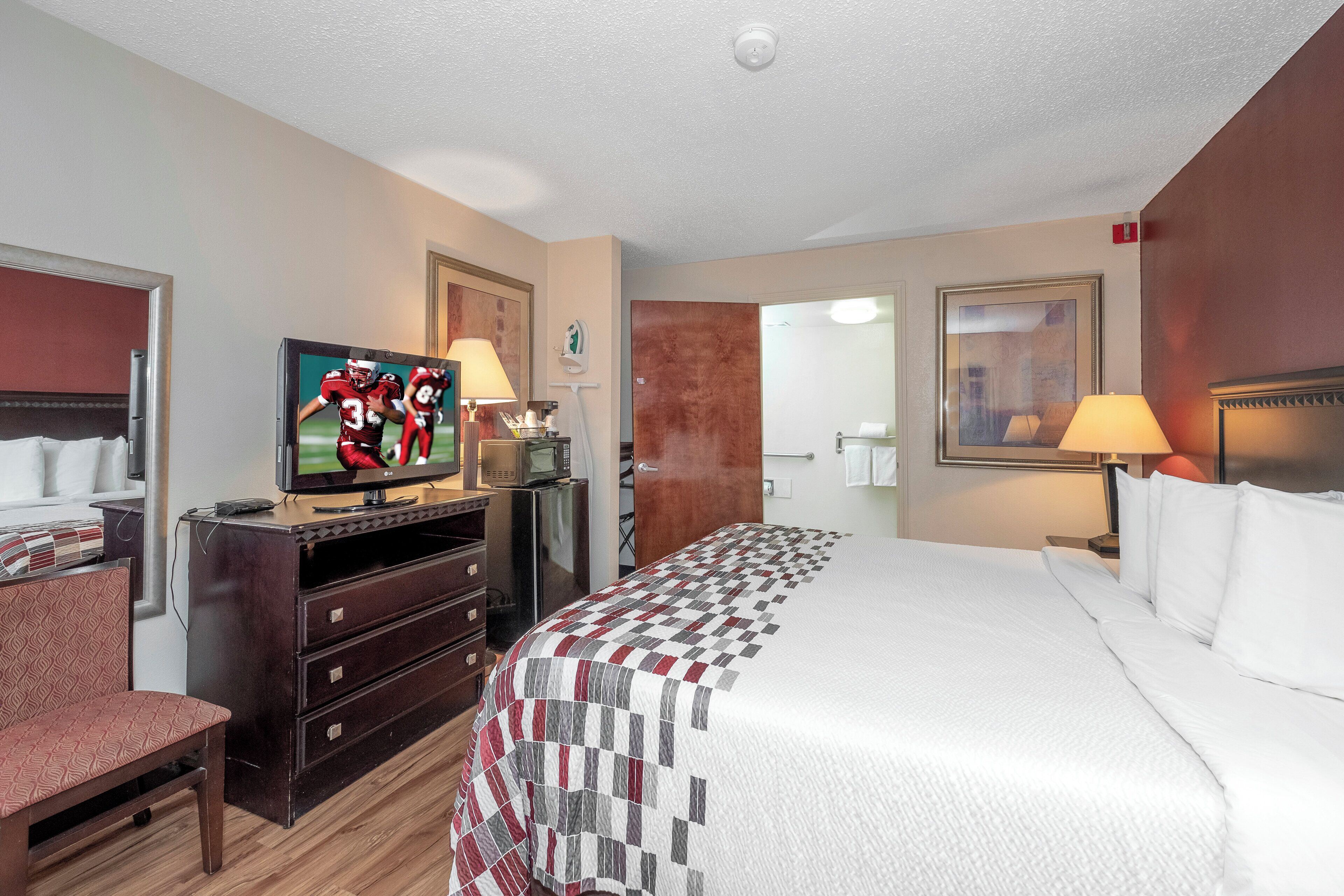 A hotel room with a bed, TV, dresser, and a door leading to a bathroom.