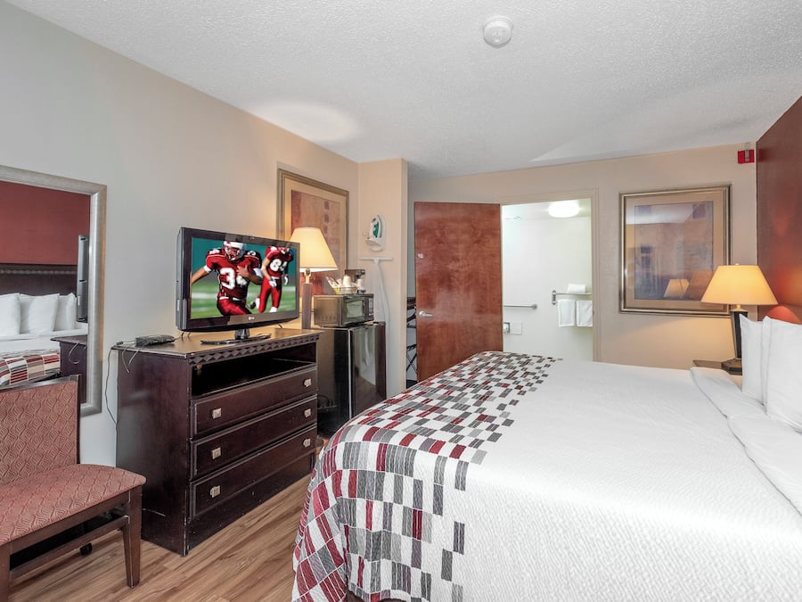 A hotel room with a bed, TV, dresser, and a door leading to a bathroom.