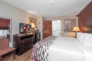 Habitación de hotel con cama, televisor, cómoda y puerta que da a un baño.