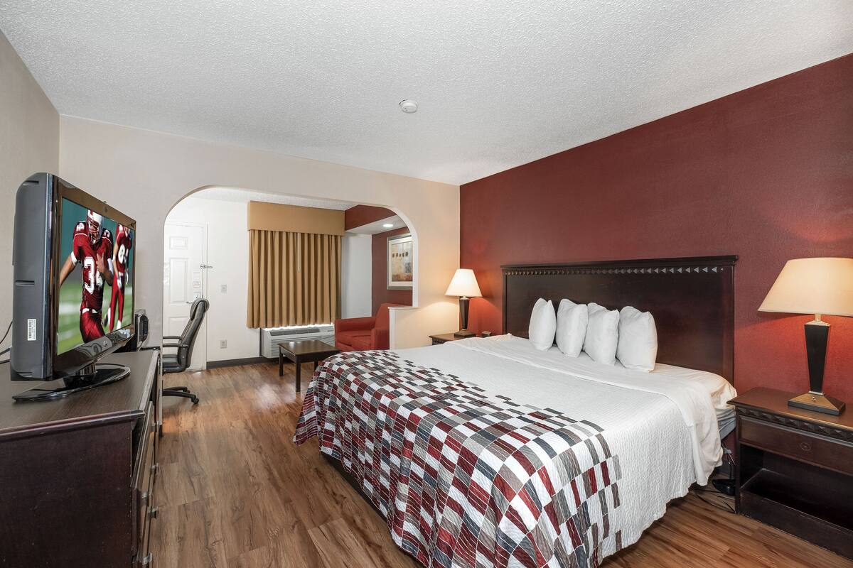 A hotel room with a large bed, a TV on a desk, a desk lamp, and a chair.