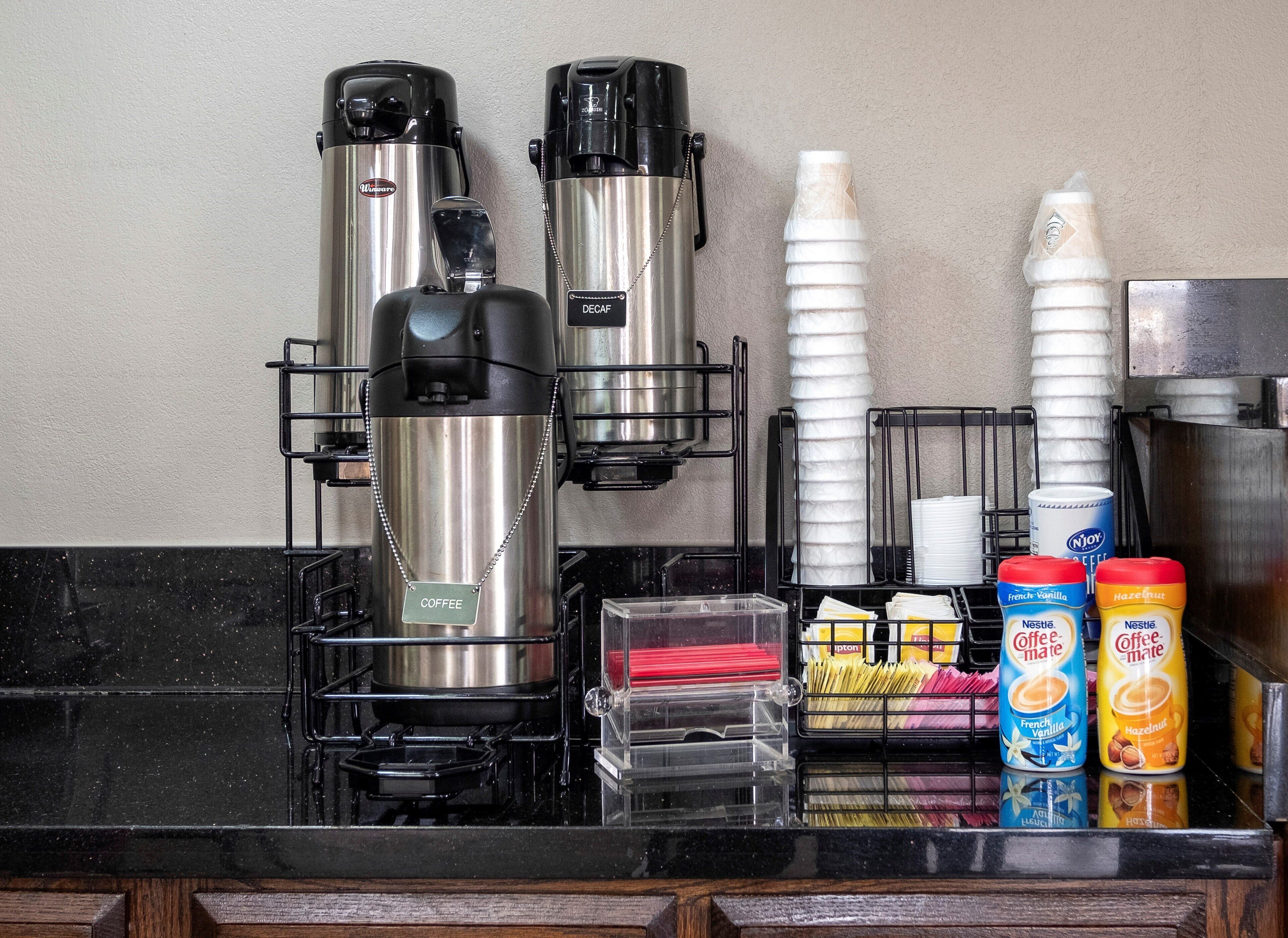 A coffee station with two coffee makers, disposable cups, and various coffee creamer options.