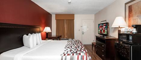Una habitación de hotel con cama, televisor, microondas, cómoda, escritorio y puerta.