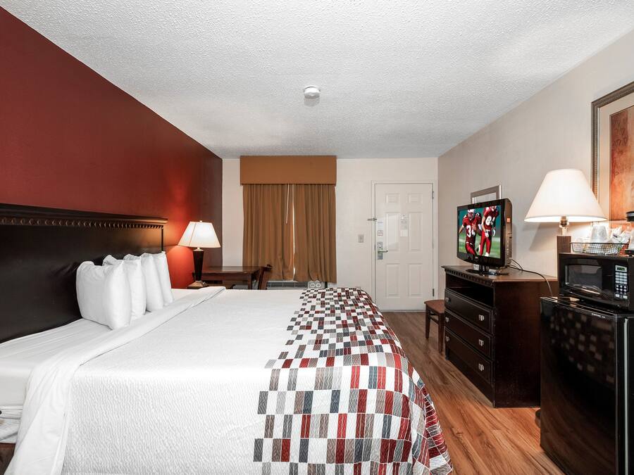 Una habitación de hotel con cama, televisor, microondas, cómoda, escritorio y puerta.
