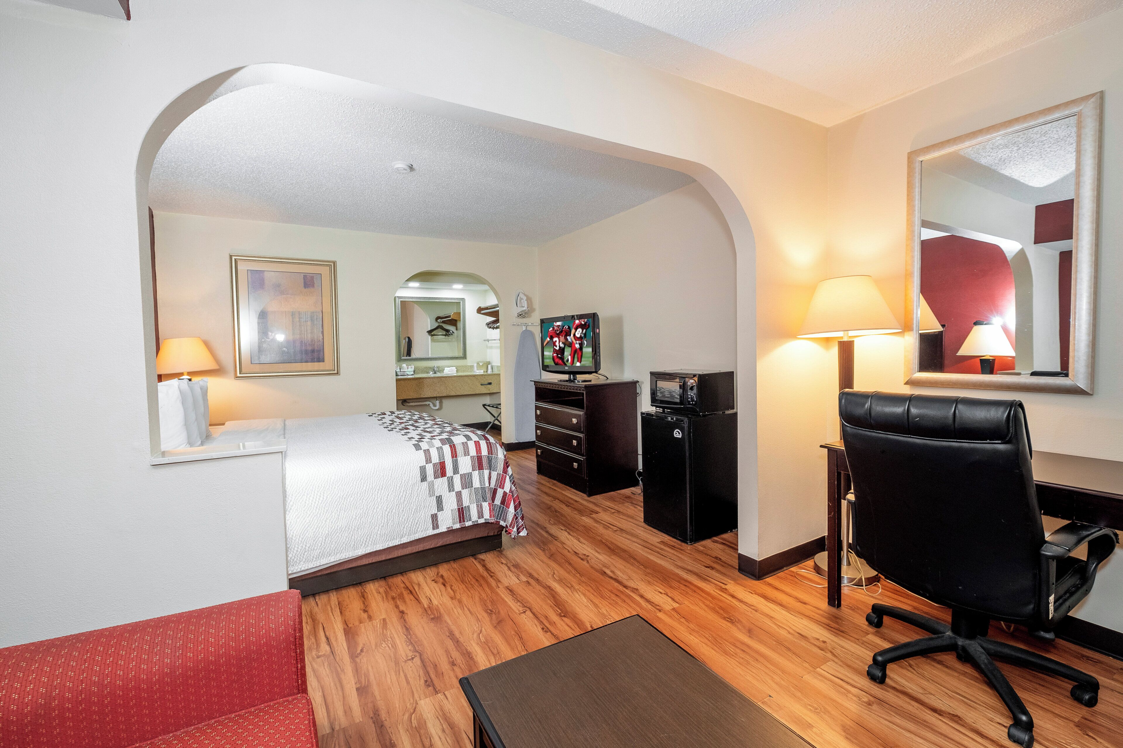 A hotel room with a bed, a desk, a chair, a TV, and a mirror.