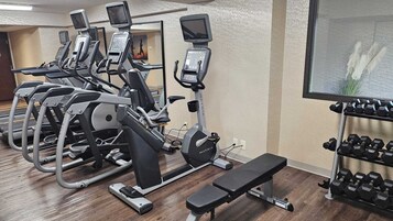 Un gimnasio con cintas de correr, una banca y un estante con mancuernas.