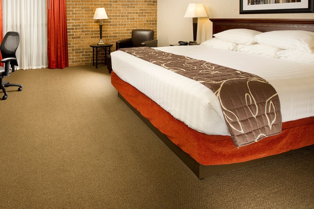 Una habitación de hotel con una cama grande, un escritorio, una silla, una lámpara y un cuadro en la pared.