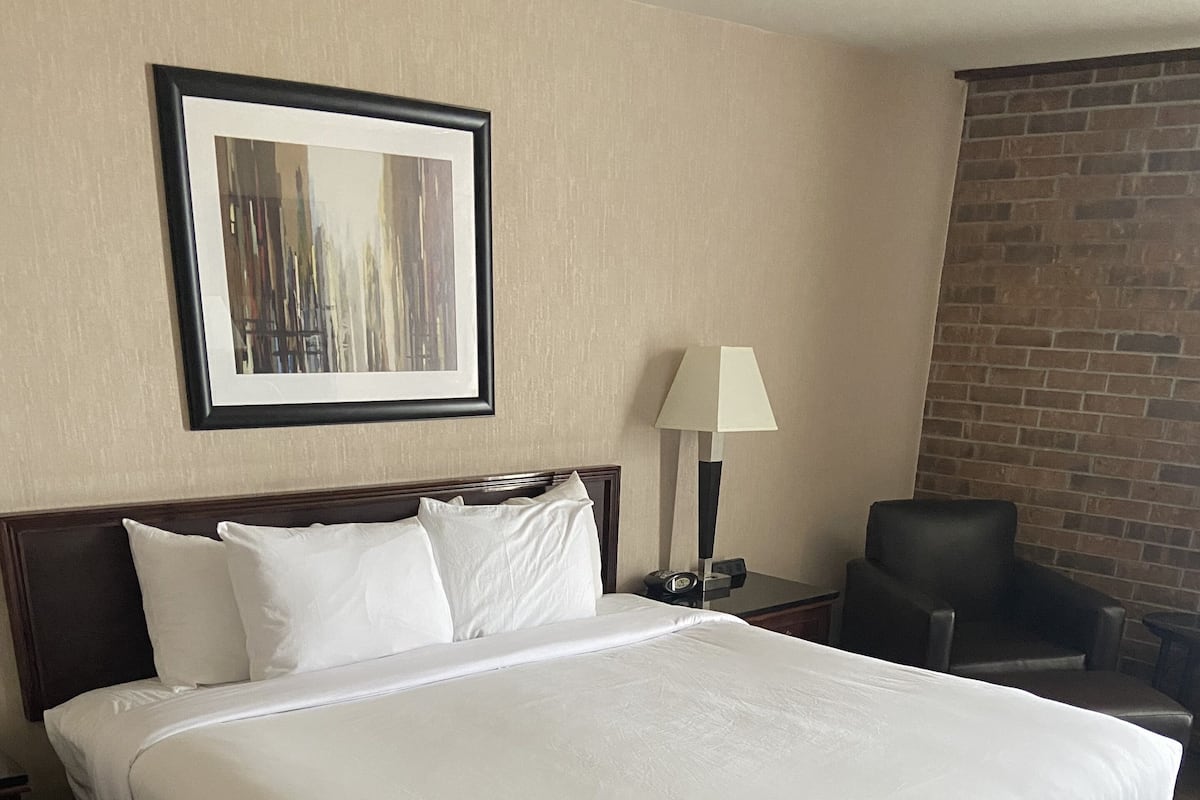 Habitación de hotel con una cama grande, una mesita de noche, una lámpara, una silla y un cuadro en la pared.