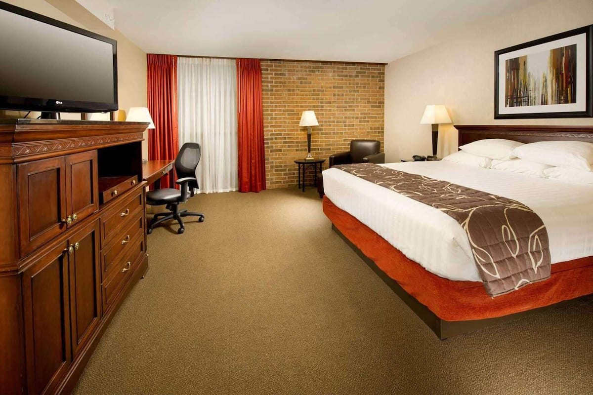 Una habitación de hotel con cama, escritorio, silla, televisor y una pared de ladrillo.