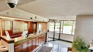 A hotel reception area with a reception desk, a sign reading "Hotel Lotus," and a view of the parking lot through the entrance. - Hotel Lotus Kansas City Merriam (Mission)