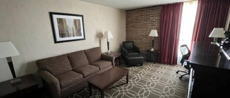 Habitación de hotel con sofá, dos sillones, una mesa de centro, escritorio y televisor.