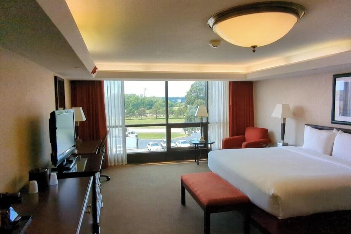 A hotel room with a large bed, a desk with a TV, a chair, and a view of the outdoors.