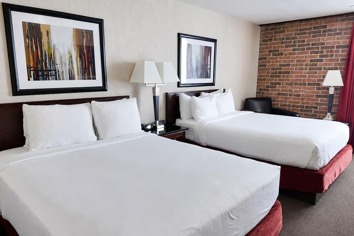 Habitación de hotel con dos camas, un muro de ladrillo y dos cuadros enmarcados en la pared.