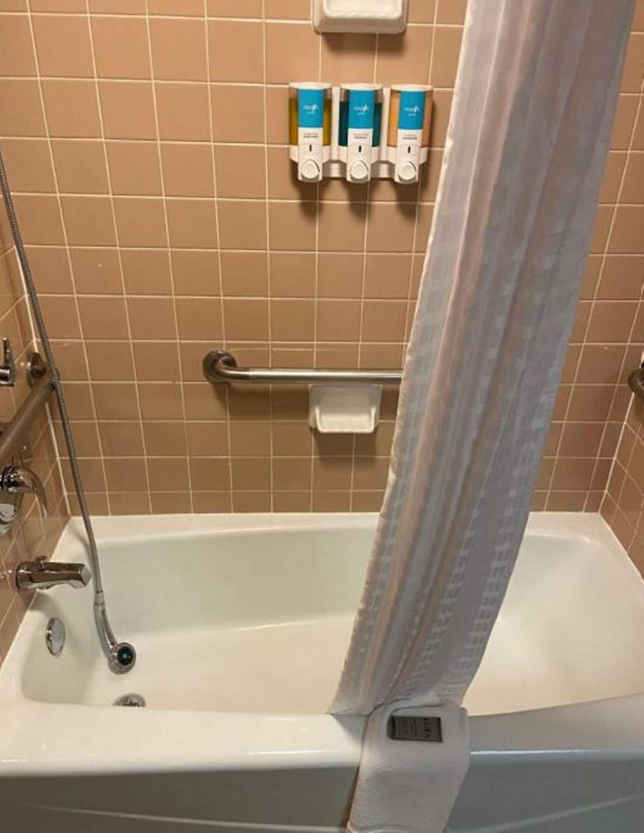 A bathroom with a bathtub, a shower, and a hand dryer mounted on the wall.