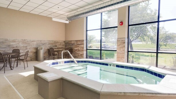 A spa area with a hot tub, seating area, and large windows offering a view of the outdoors. - Hotel Lotus Kansas City Merriam (Mission)