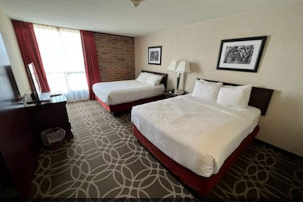 Habitación de hotel con dos camas, un escritorio, una silla, una lámpara y un cuadro en la pared.