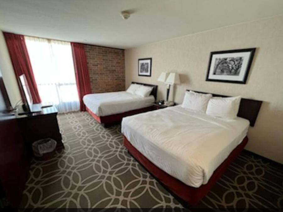 A hotel room with two beds, a desk, a chair, a lamp, and a picture on the wall.