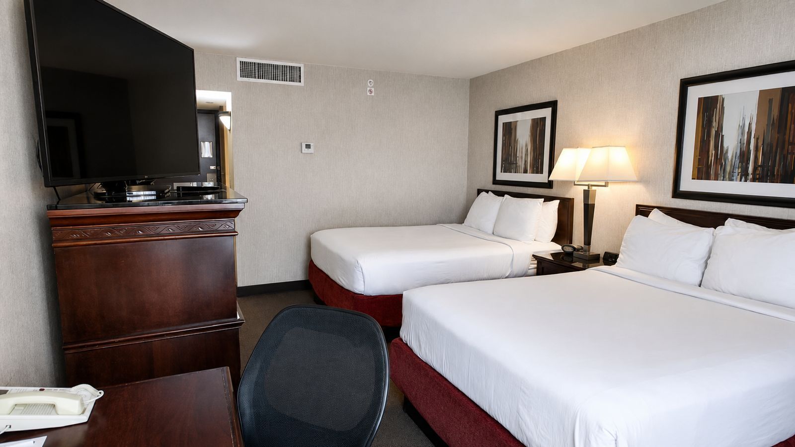 Une chambre d’hôtel avec deux lits, un bureau, une chaise, une télévision et une lampe.