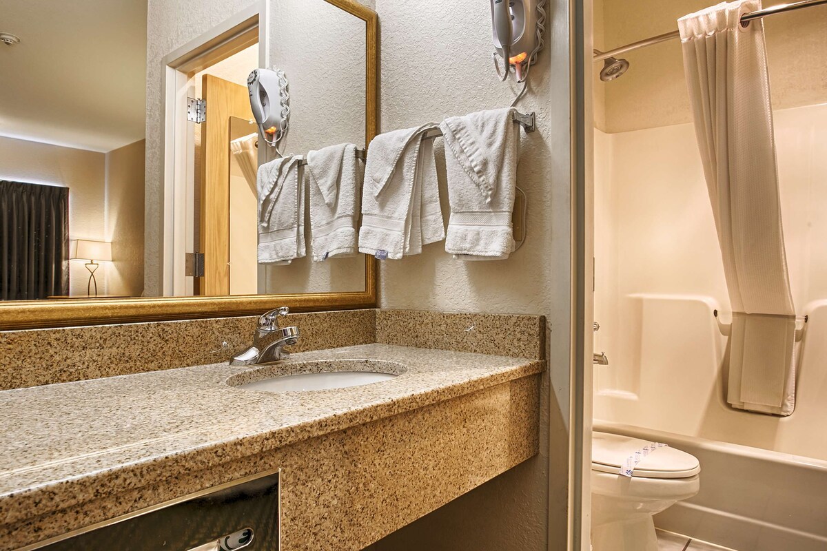 A bathroom with a granite countertop sink, a mirror, a towel rack with multiple towels, a shower curtain, and a toilet.