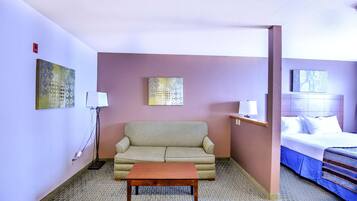 A hotel room with a beige sofa, a wooden table, a bed with white linens, and two wall-mounted lamps.