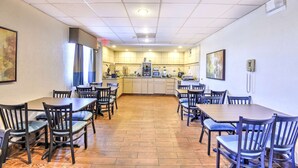 A dining area with multiple tables and chairs, a kitchen in the background, and a ceiling with recessed lighting.