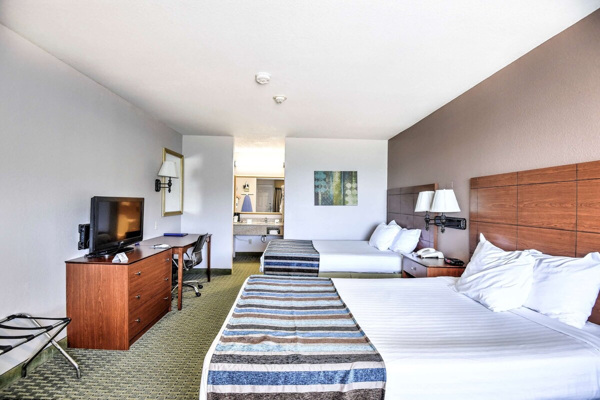 A hotel room with a bed, a desk with a computer, a television, a dresser, and a bathroom visible in the background.