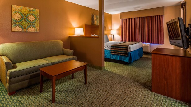A hotel room with a sofa, a small table, a bed with a blue bedspread, a television, and a wall-mounted artwork.